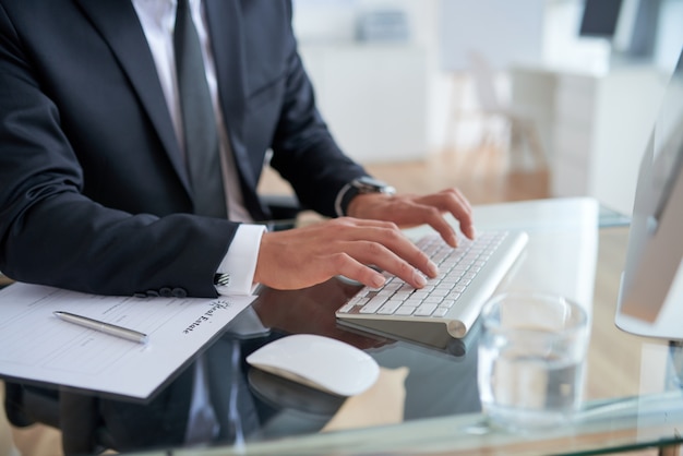 Hombre de negocios irreconocible escribiendo en el teclado en la oficina