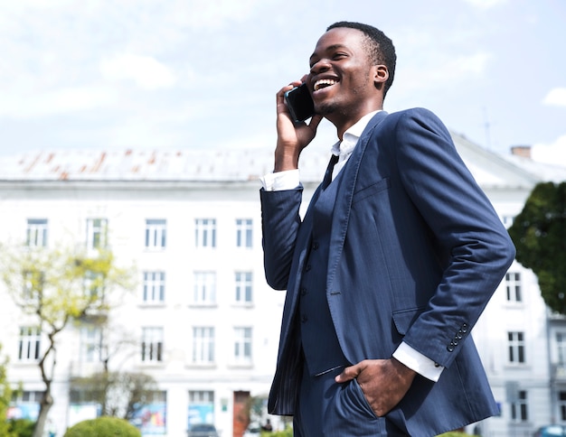 Hombre de negocios joven acertado con las manos en su bolsillo que habla en el teléfono móvil
