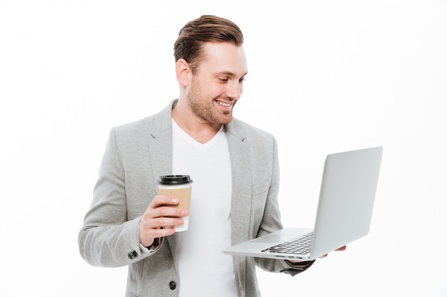 Hombre de negocios joven alegre que bebe el café usando la computadora portátil