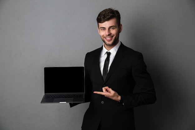 Hombre de negocios joven alegre que muestra la pantalla de la computadora portátil