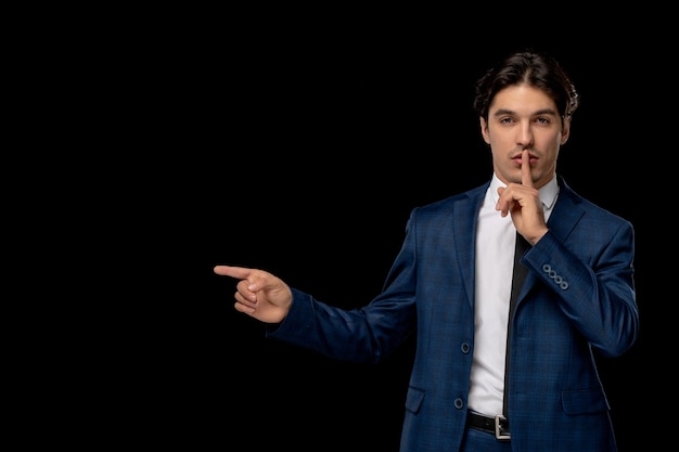 Hombre de negocios joven apuesto en traje azul oscuro con corbata mostrando gesto de silencio