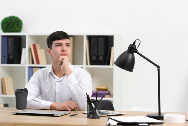 Hombre de negocios joven contemplado que se sienta en el lugar de trabajo en la oficina