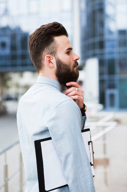 Foto gratuita hombre de negocios joven contemplado con el tablero que toca su barba