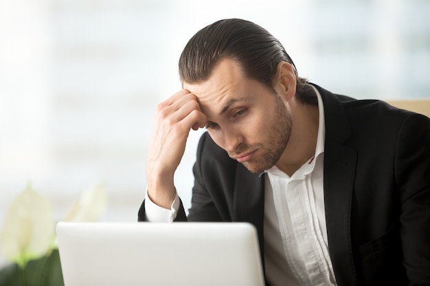 Hombre de negocios joven desconcertado que mira la pantalla de la computadora portátil