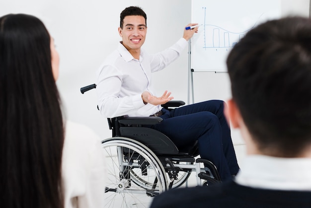 Foto gratuita hombre de negocios joven discapacitado que se sienta en la silla de ruedas que da presentación a su colega en la oficina