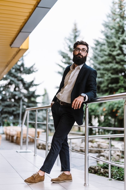 Hombre de negocios joven elegante que se coloca cerca de la verja que mira lejos