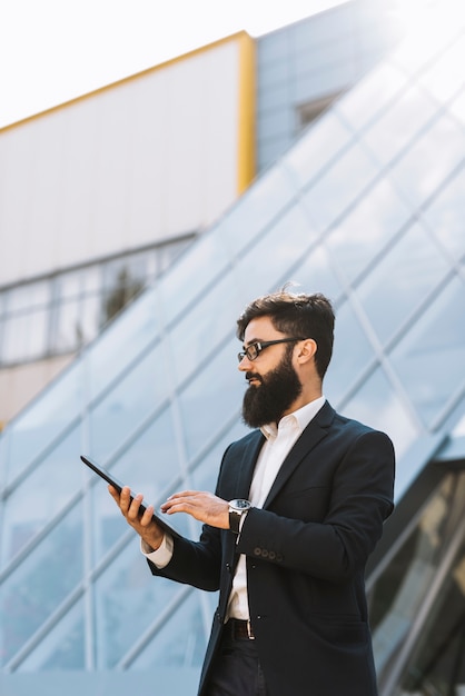 Hombre de negocios joven elegante que usa la tableta digital en el aire libre