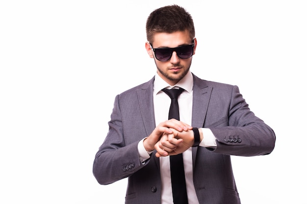 Hombre de negocios joven con gafas de sol comprobando el tiempo de su reloj de pulsera aislado sobre fondo blanco.