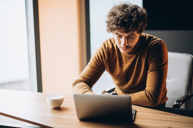 Hombre de negocios joven guapo trabajando en la computadora y tomando café