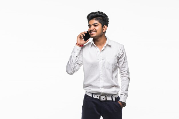 Hombre de negocios joven indio que habla en teléfono móvil en la pared blanca.
