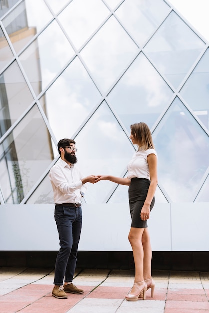 Hombre de negocios joven que sacude la mano con la empresaria delante del edificio moderno