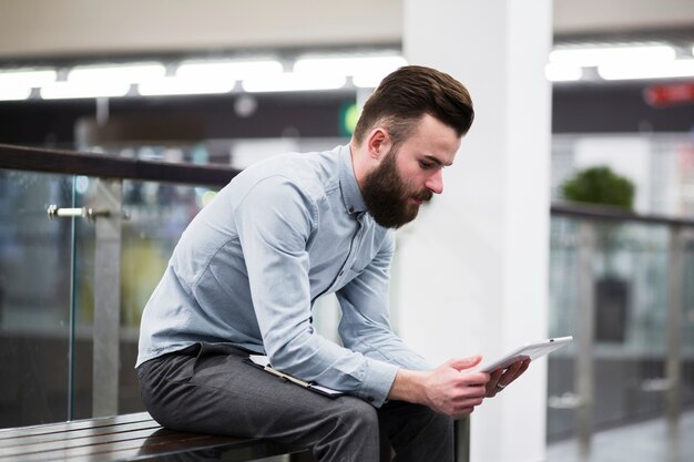 Hombre de negocios joven que se sienta en banco usando la tableta digital