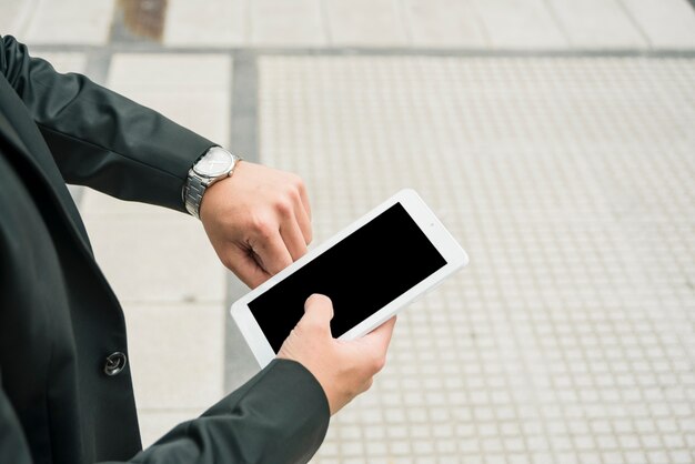 Hombre de negocios joven que sostiene el smartphone que comprueba el tiempo en el reloj