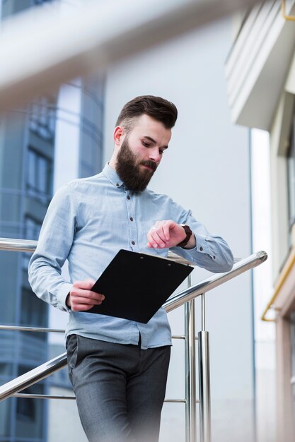 Hombre de negocios joven que sostiene el tablero disponible que comprueba tiempo