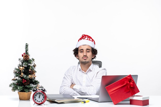 Hombre de negocios joven serio ocupado con sombrero de santa claus divertido posando para la cámara en la oficina sobre fondo blanco