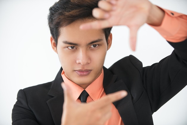 Hombre de negocios joven serio que muestra el marco del dedo