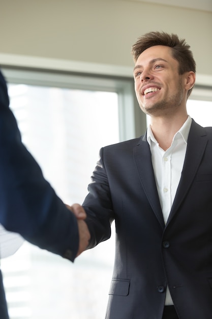 Foto gratuita hombre de negocios joven sonriente que lleva el traje negro que sacude la mano masculina,