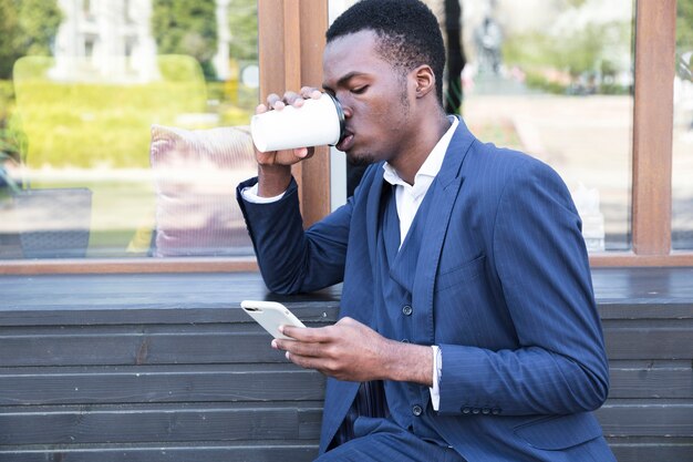 Hombre de negocios joven sonriente que se sienta en el banco que bebe el café