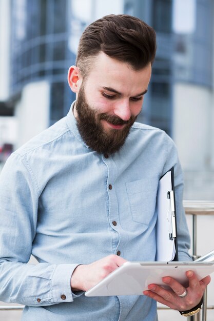 Hombre de negocios joven sonriente que sostiene el tablero usando la tableta digital