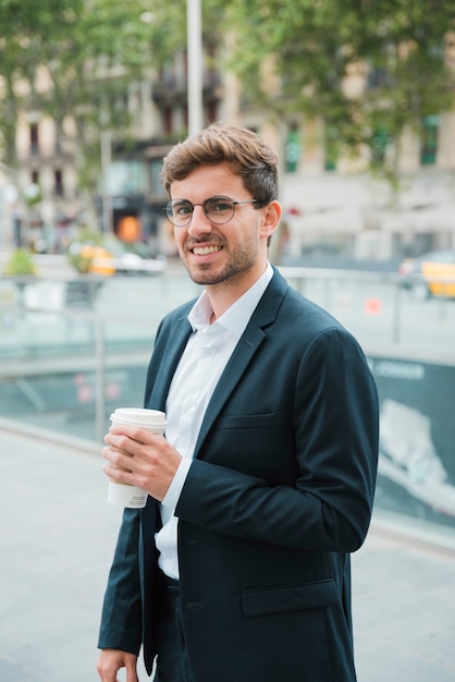 Foto gratuita hombre de negocios joven sonriente que sostiene la taza de café para llevar disponible