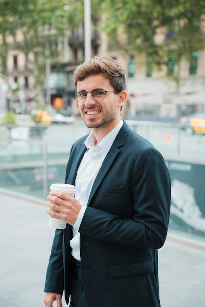 Hombre de negocios joven sonriente que sostiene la taza de café para llevar disponible