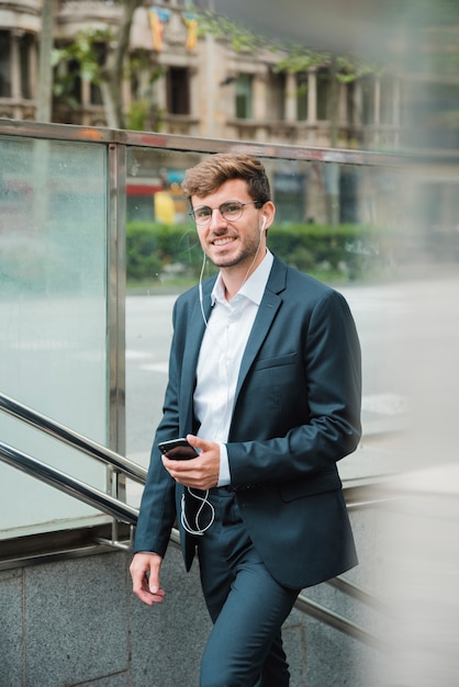 Foto gratuita hombre de negocios joven sonriente con su auricular en el oído que sostiene el teléfono móvil disponible