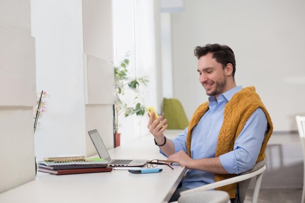 Hombre de negocios joven con teléfono móvil y sentado frente a su computadora portátil mientras está sentado en la cafetería. Freelancer masculino que trabaja en el panel táctil de la computadora.