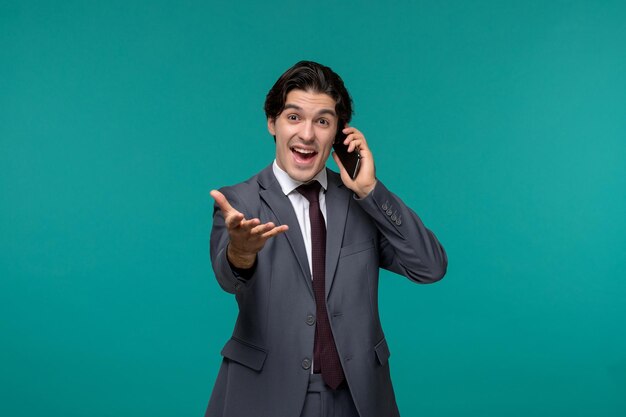 Hombre de negocios lindo joven guapo en traje de oficina gris y corbata feliz hablando por teléfono