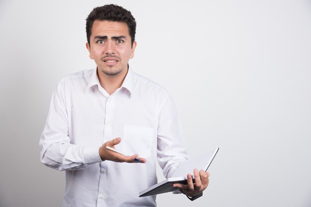 Hombre de negocios loco apuntando al cuaderno sobre fondo blanco.