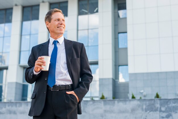 Hombre de negocios maduro feliz con la taza de café delante del edificio