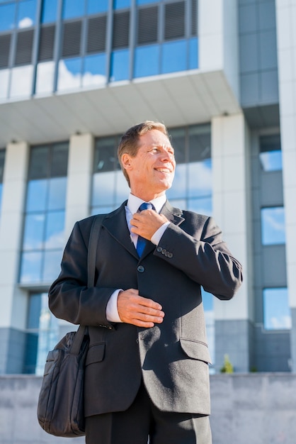 Hombre de negocios maduro feliz en traje negro con el edificio de oficinas en fondo