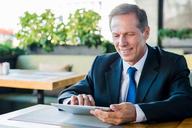 Hombre de negocios maduro sonriente que trabaja en la tableta digital en restaurante