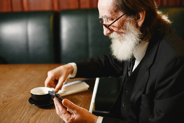 Hombre de negocios mayor barbudo. Hombre con café. Senior en traje negro.