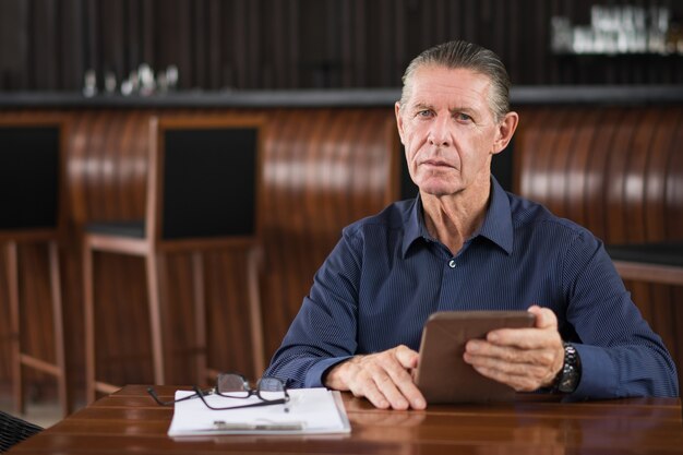 El hombre de negocios mayor que trabaja en la tableta en el Café