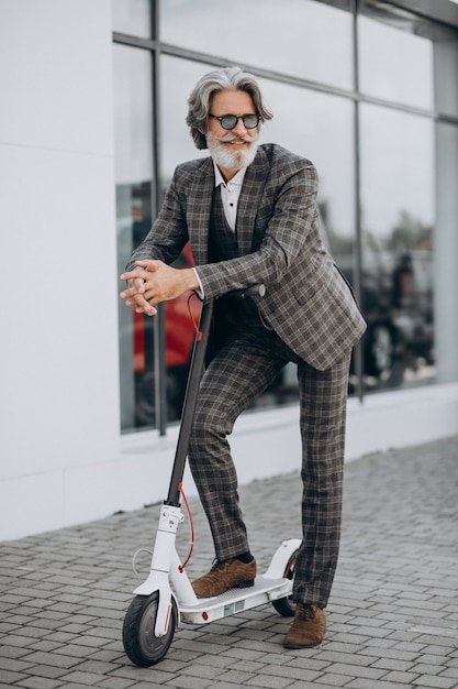 Foto gratuita hombre de negocios de mediana edad montando scooter en un elegante traje