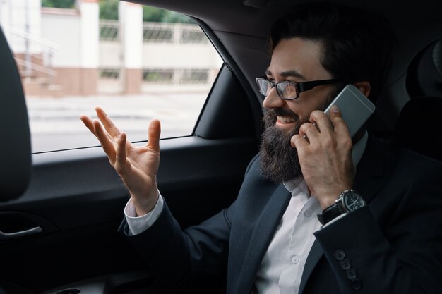 Un hombre de negocios mientras viaja en automóvil en el asiento trasero con un teléfono inteligente