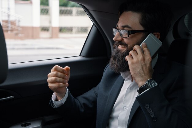 Un hombre de negocios mientras viaja en automóvil en el asiento trasero con un teléfono inteligente