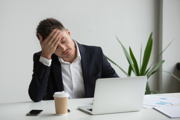 Hombre de negocios del milenio frustrado que tiene fuerte dolor de cabeza cansado de trabajo portátil