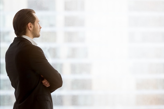 Foto gratuita el hombre de negocios mira soñador en ventana en la oficina