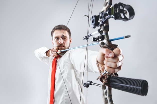 Hombre de negocios con el objetivo de objetivo con arco y flecha, aislado sobre fondo gris de estudio. El negocio, el objetivo, el desafío, la competencia, el concepto de logro.