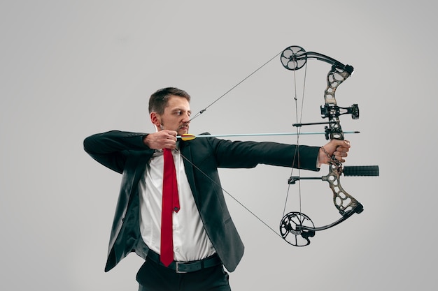 Hombre de negocios con el objetivo de objetivo con arco y flecha, aislado sobre fondo gris.