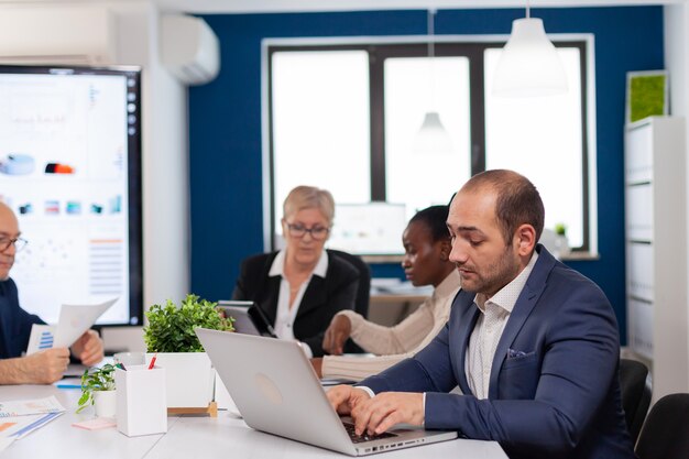 Hombre de negocios ocupado usando laptop escribiendo sentado en la mesa de conferencias en la sala amplia concentrado en el trabajo