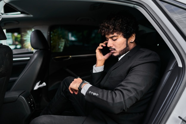 Hombre de negocios de pelo rizado en el asiento trasero hablando por teléfono.