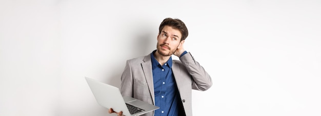 Un hombre de negocios pensativo se rasca la cabeza y mira hacia otro lado tomando una decisión mientras trabaja en una computadora portátil de pie