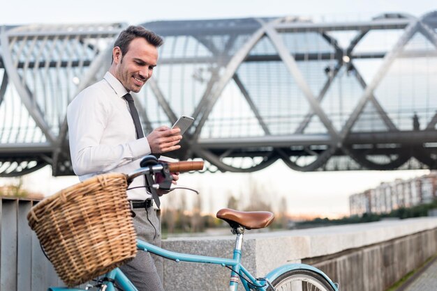 Hombre de negocios de pie junto a su bicicleta vintage hablando por teléfono móvil