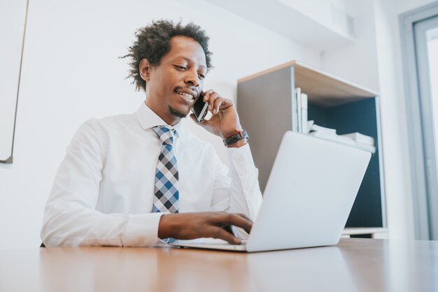 Hombre de negocios profesional hablando por teléfono y usando su computadora portátil mientras trabajaba en la oficina. Concepto de negocio