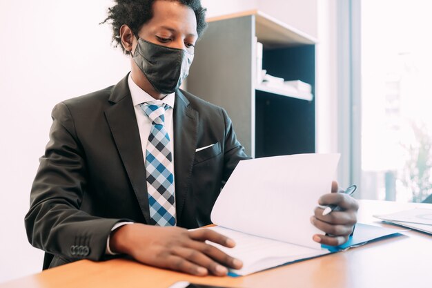 Hombre de negocios profesional con mascarilla mientras trabaja con algunos archivos y documentos en su oficina.