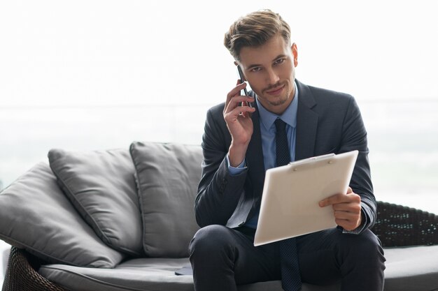 El hombre de negocios que invita al teléfono y sienta en el sofá