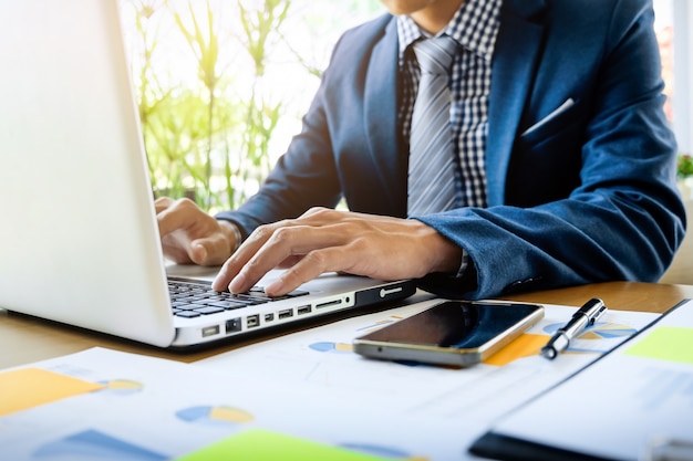 Hombre de negocios que trabaja en la oficina con la computadora portátil, la tableta y los documentos de datos del gráfico en su escritorio