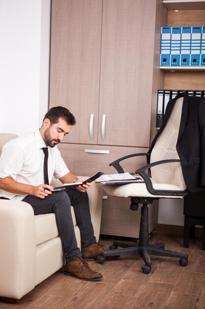 Hombre de negocios que trabaja en la oficina en el sofá poniendo largas horas de trabajo. Empresario en entorno profesional